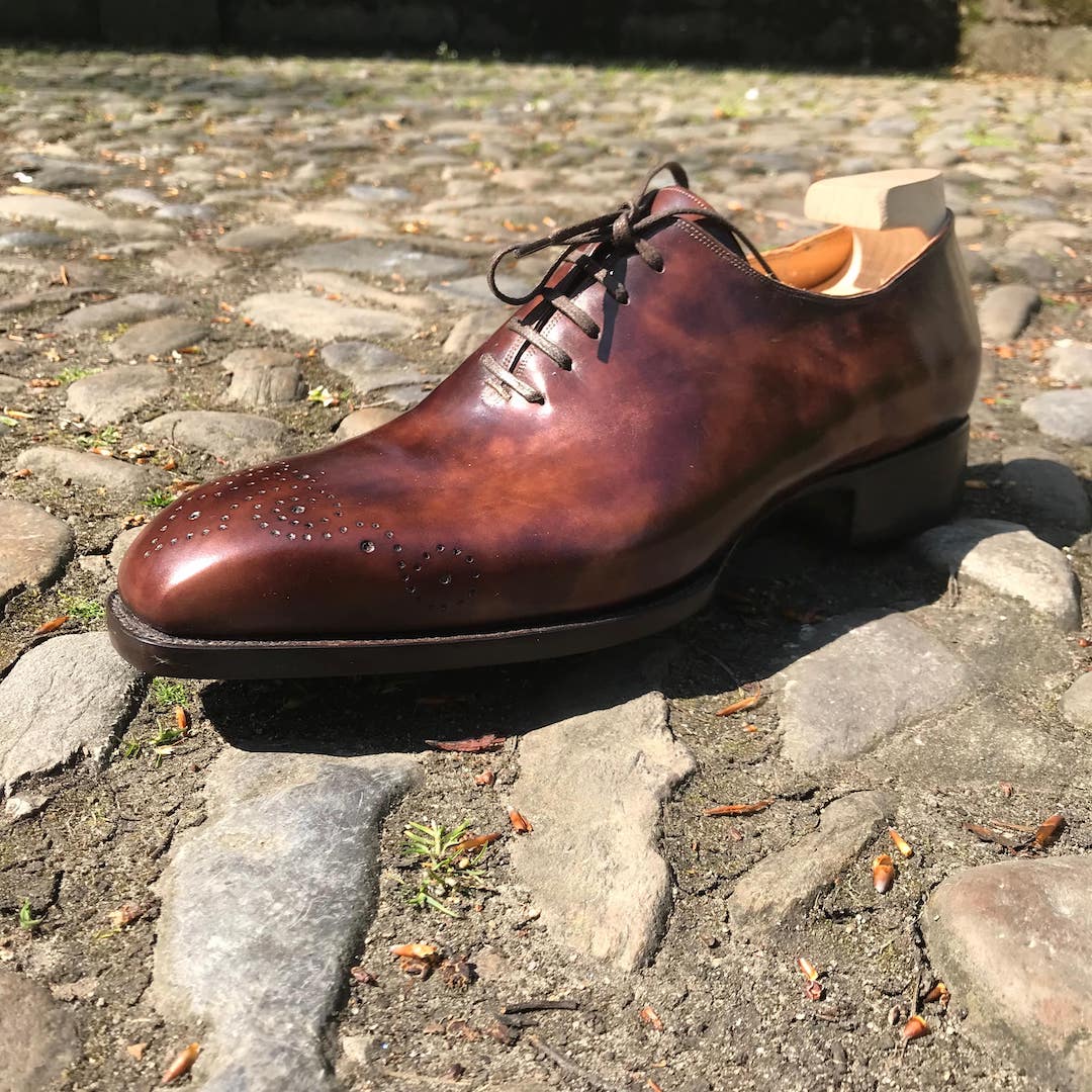 brown hand punched toe medallion shoes on cobble stones